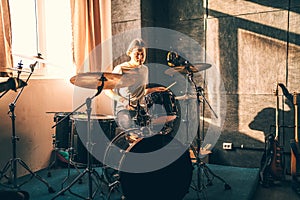 Drummer plays drums in music studio at band rehearsal. Musician with instrument in beautiful sunset light from window