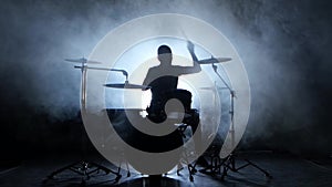 Drummer plays the melody on the drums energetically. Black background. Silhouette