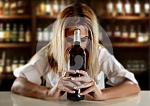 Drunk alcoholic blond woman alone in wasted depressed with red wine bottle in bar