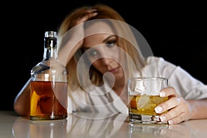 Drunk alcoholic woman wasted and depressed holding scotch whiskey glass looking thoughtful to bottle