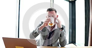 Drunk businessman drinking whiskey with glass in front of laptop at workplace 4k movie slow motion