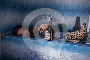 Drunk girl lying in a bathtub with a bottle in her hand