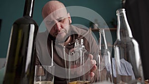 Drunk man between empty bottles sitting at a table. Alcoholism