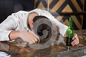 Drunk man lying on a counter with bottle of beer