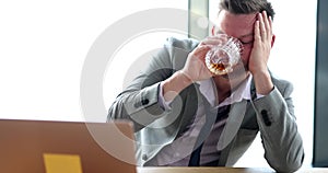 Drunk sad businessman holding glass with alcohol at workplace