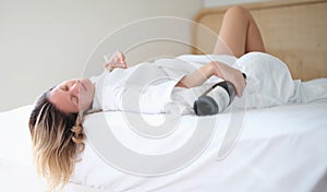 Drunk woman in bathrobe sleeps on bed with bottle of wine and glass in hotel room