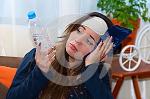 Drunk woman with a sleeping eye mask in her head and aplying a bag of ice in her head using her hand and holding a photo