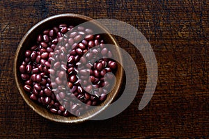 Dry adzuki beans in dark wooden bowl isolated on dark brown wood