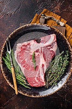 Dry aged Raw porterhouse beef meat Steak, fresh T bone on rustic plate with spices. Dark background. Top view