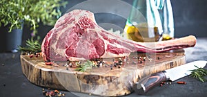 Dry aged raw tomahawk beef steak with ingredients for grilling.