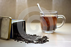 Dry black tea spilled from a box and a glass mug with tea on the table