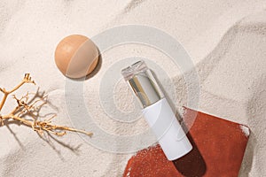 A dry branch, a wooden ball, an unlabeled cosmetic bottle and a notebook stand out against the smooth sand background. Concept of