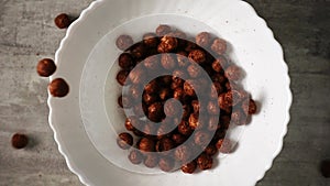 Dry breakfast consisting of chocolate cornflakes is falling in slowmo into a white dish