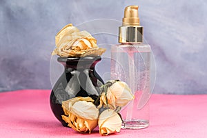 Dry buds of yellow roses on pink table. Perfume bottles for cosmetics. Presentation of new fragrance