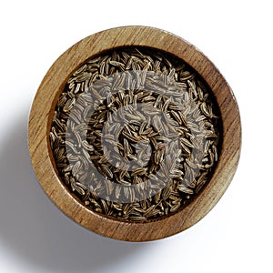 Dry caraway or cumin seeds in dark wood bowl isolated on white.