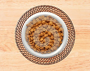 Dry cat food in plate on wicker placemat on wooden background