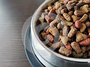 Dry cat food in a stainless steel bowl on wood table.