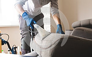 Dry cleaner`s man employee removing dirt from furniture in flat, closeup, vacuum clean sofa with professional equipment