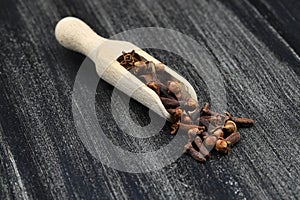 Dry cloves in wooden scoop isolated on wooden background with clipping path. Top view. Flat lay. selective focus