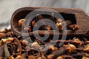 Dry cloves in wooden scoop isolated on wooden background with clipping path. Top view. Flat lay. selective focus