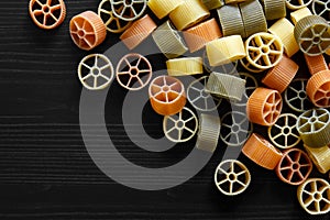 Dry coloured wagon wheel pasta on black textured wood, from abov