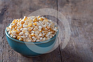 Dry corn kernels in a green bowl, set on wooden table