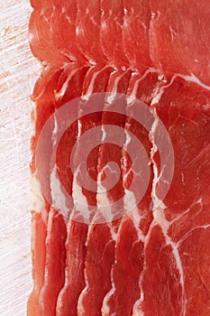 Dry cured ham slices on white wood background