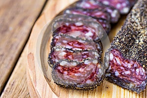 Dry-cured sausage coated with black pepper crust sliced on wood cutting board. Traditional Spanish or mediterranean delicacy.