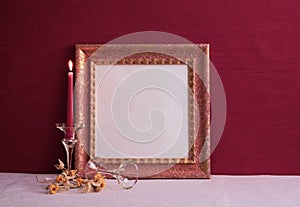 Dry daffodils, a long-stemmed candlestick and a candle is burning, an old photo frame on a red background