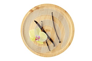 Dry dark brown vanilla pods and yellow orchid flower on bamboo wooden plate isolated on white background. Aromatic vanilla sticks