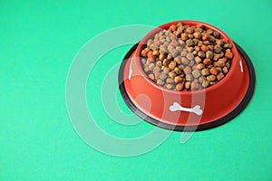 Dry dog food in feeding bowl on green background. Space for text