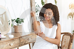 Dry Elbows Treatment. Smiling Black Woman Applying Moisturising Cream At Home