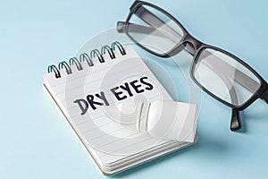 Dry eyes concept with eye drops and eyeglasses on blue background