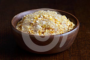 Dry flaked corn in brown wooden bowl.