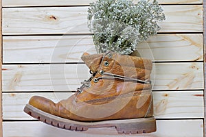 Dry flowers in boots on woodback ground .