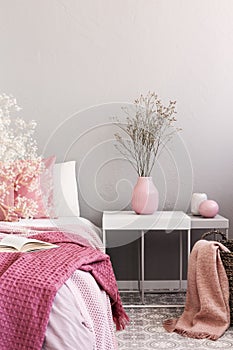 Dry flowers in pastel pink vase on simple nightstand table next to bed