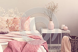 Dry flowers in pastel pink vase on simple nightstand table next to bed
