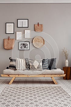 Dry flowers in white vase on small wooden table behind comfortable futon sofa with pillows