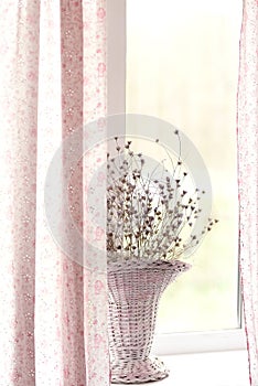 Dry flowers in a wicker basket on a light window.