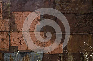 Dry grass near the rust and oxidized wall. Old iron panel. The wall of rusted plates. Grunge rusted metal abstract texture. Rusted