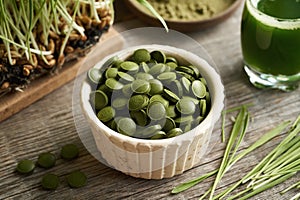 Dry green barley grass tablets rich in chlorophyll with fresh blades and juice in the background