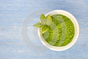 Dry green tea powder matcha tea with whole leaves in a white Cup, isolated on a blue background