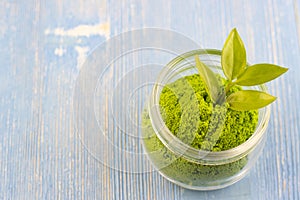 Dry green tea powder matcha tea with whole leaves in a white Cup, isolated on a blue background