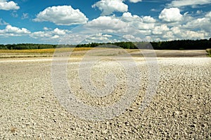 Dry ground on a plowed field in front of a forest and clouds on the sky