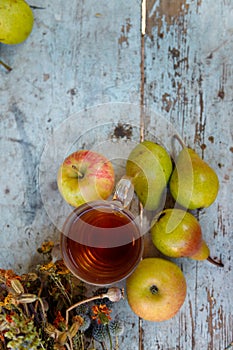 Dry healing herbs bouquet, cup of herbal tea and some fresh fruits, apples and pears on rustic background.