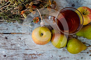 Dry healing herbs bouquet, cup of herbal tea and some fresh fruits, apples and pears on rustic background.