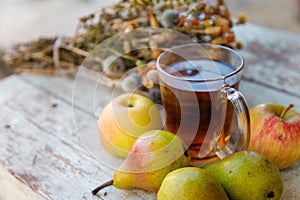 Dry healing herbs bouquet, cup of herbal tea and some fresh fruits, apples and pears on rustic background.