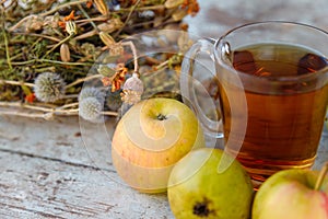 Dry healing herbs bouquet, cup of herbal tea and some fresh fruits, apples and pears on rustic background.