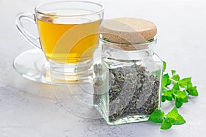 Dry herbal mint tea in a jar with cup of tea on background