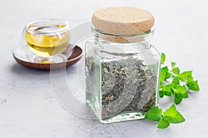Dry herbal mint tea in jar with cup of tea on background, horizontal